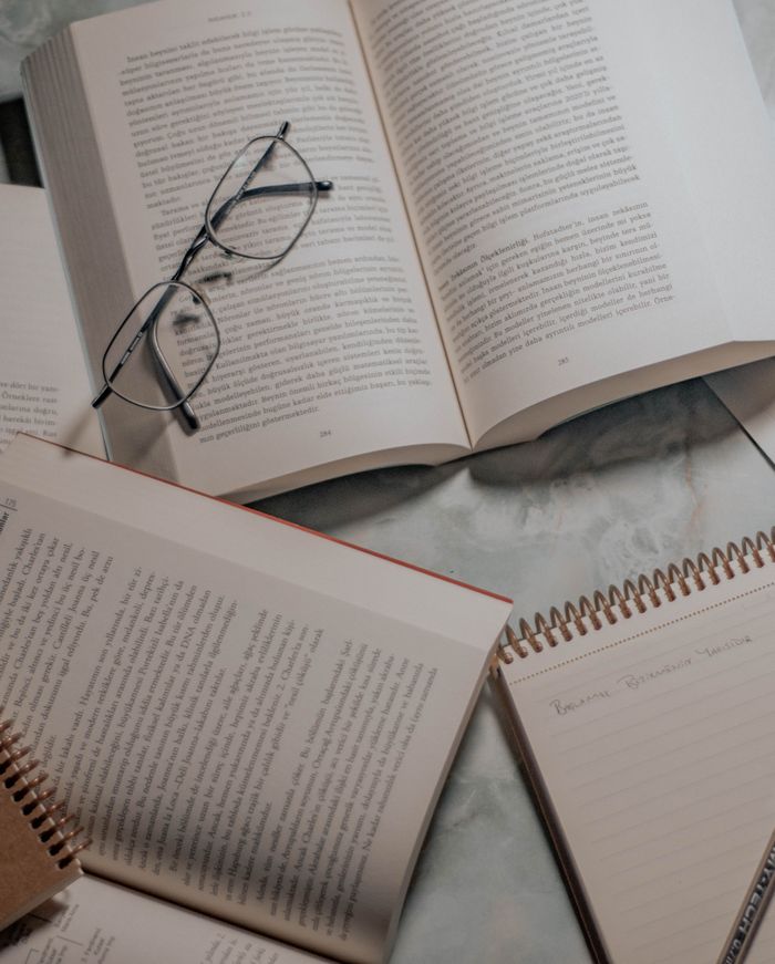 our-story-01 Open books and glasses on a marble table, with notepad for study or research context.