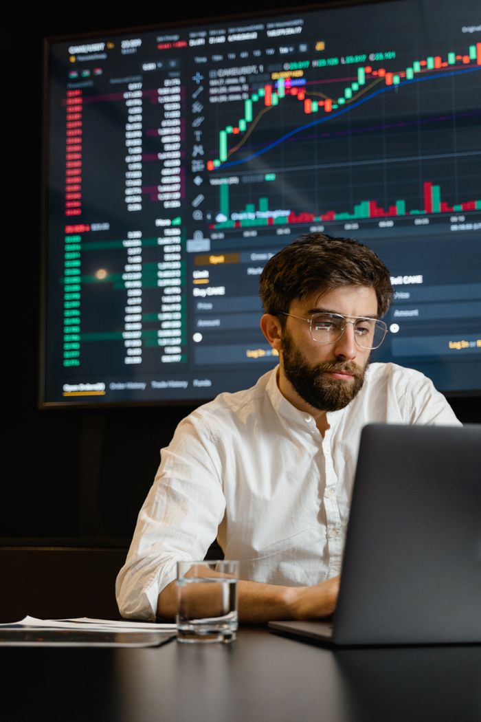 services-06 A man analyzing cryptocurrency trends on a laptop with trading graphs displayed on a screen.